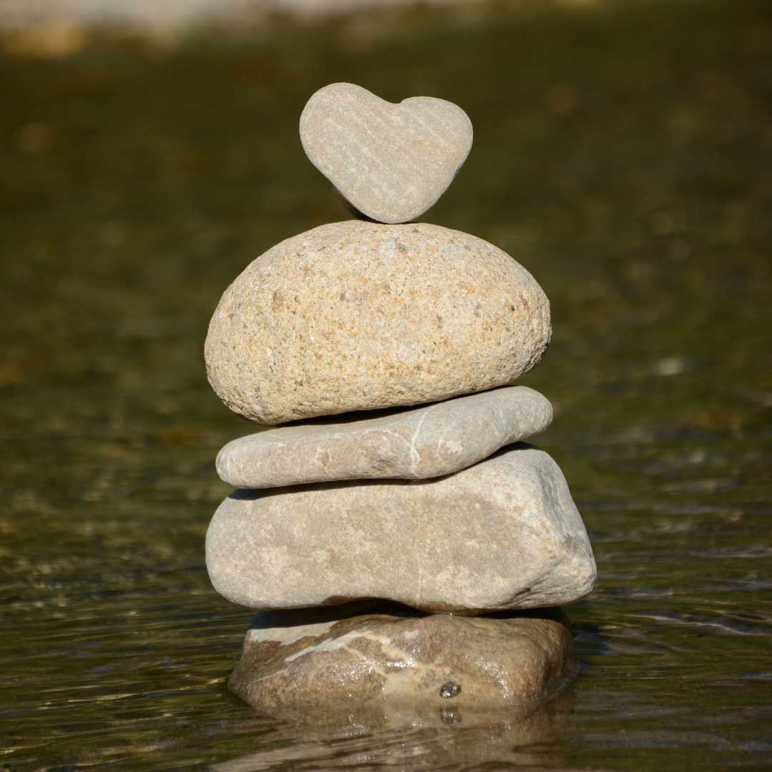 Stack of stones in a river with a heart shaped stone on top